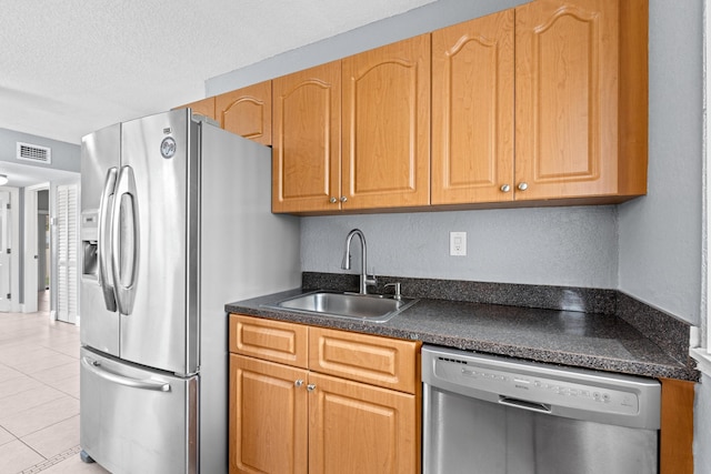 kitchen with light tile patterned flooring, stainless steel appliances, a sink, visible vents, and dark countertops