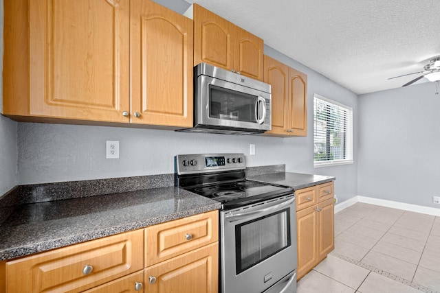 kitchen featuring light tile patterned floors, dark countertops, ceiling fan, appliances with stainless steel finishes, and a textured ceiling