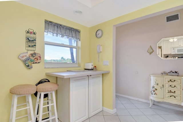 kitchen featuring light tile patterned floors, white microwave, a breakfast bar, visible vents, and baseboards