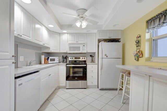 kitchen featuring white appliances, a raised ceiling, light countertops, white cabinetry, and a sink