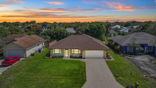 ranch-style home with a shingled roof, concrete driveway, a lawn, an attached garage, and a residential view