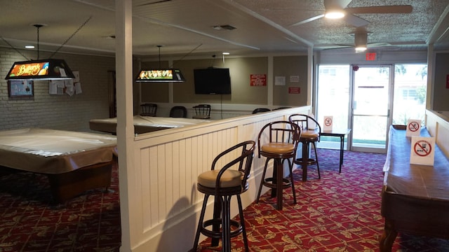 bar with a textured ceiling, brick wall, carpet flooring, visible vents, and a ceiling fan