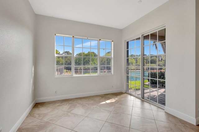 empty room featuring a wealth of natural light, baseboards, and light tile patterned floors