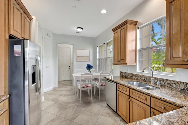 kitchen with plenty of natural light, brown cabinetry, stainless steel appliances, stone counters, and a sink