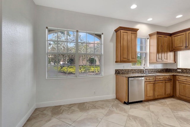 kitchen featuring baseboards, dishwasher, brown cabinets, dark stone countertops, and a sink