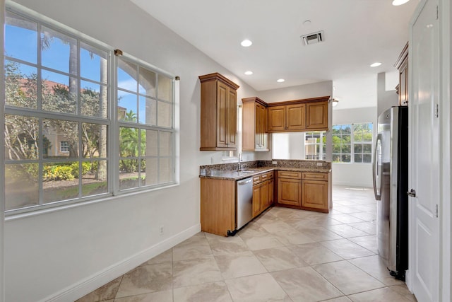 kitchen with stainless steel appliances, brown cabinetry, a sink, and visible vents