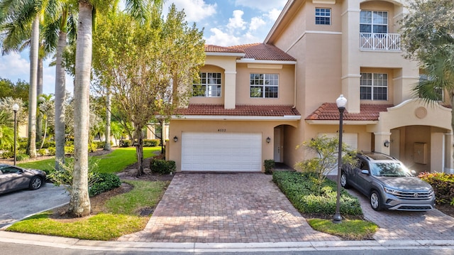 view of front of home with decorative driveway, a tile roof, an attached garage, and stucco siding