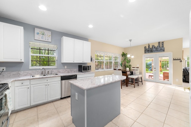 kitchen with stainless steel appliances, a kitchen island, a sink, white cabinetry, and french doors