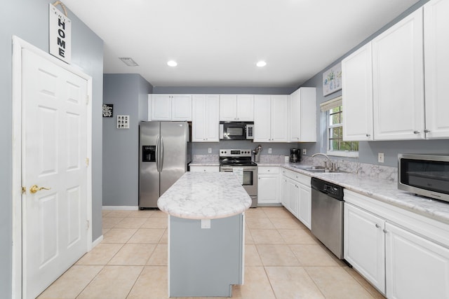 kitchen with light tile patterned floors, a kitchen island, a sink, white cabinets, and appliances with stainless steel finishes