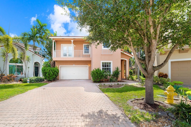 view of front of home with a balcony, a garage, decorative driveway, stucco siding, and a front yard