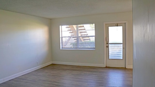 unfurnished room with a textured ceiling, baseboards, and wood finished floors