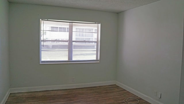 spare room featuring dark wood-style floors, a textured ceiling, baseboards, and a wealth of natural light