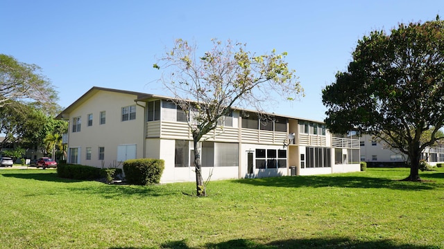 back of house featuring a sunroom, a lawn, and stucco siding