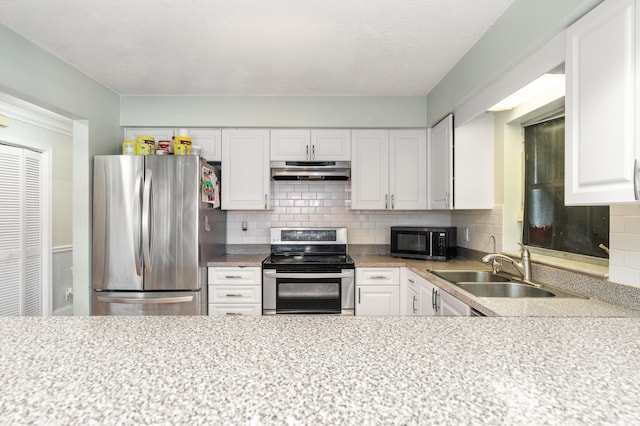 kitchen with under cabinet range hood, a sink, light countertops, appliances with stainless steel finishes, and backsplash