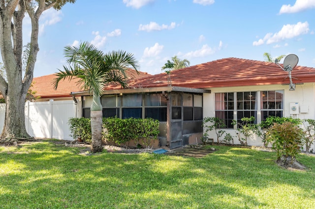 back of house with a tile roof, a yard, stucco siding, a sunroom, and fence