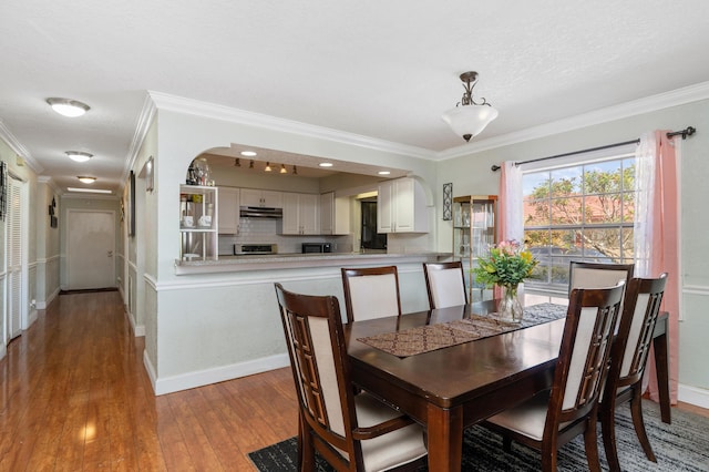 dining space featuring ornamental molding, arched walkways, baseboards, and hardwood / wood-style floors