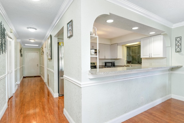 interior space with crown molding, backsplash, appliances with stainless steel finishes, a textured ceiling, and wood finished floors