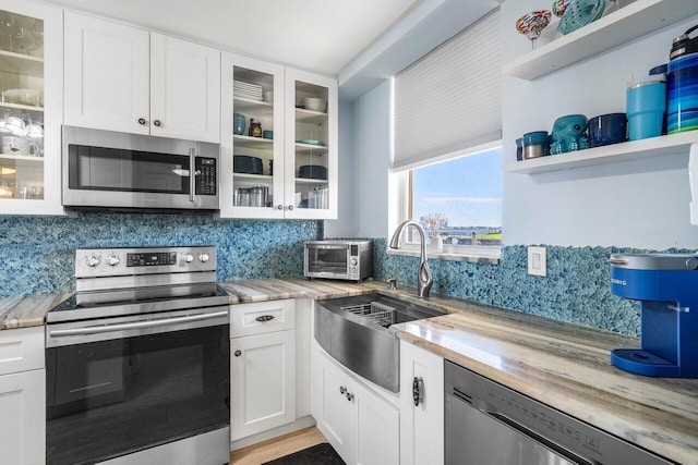 kitchen with stainless steel appliances, backsplash, a sink, and white cabinetry