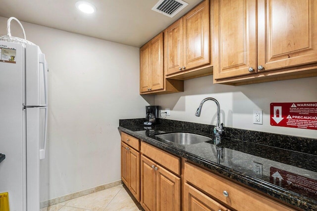 kitchen featuring visible vents, dark stone countertops, freestanding refrigerator, a sink, and light tile patterned flooring