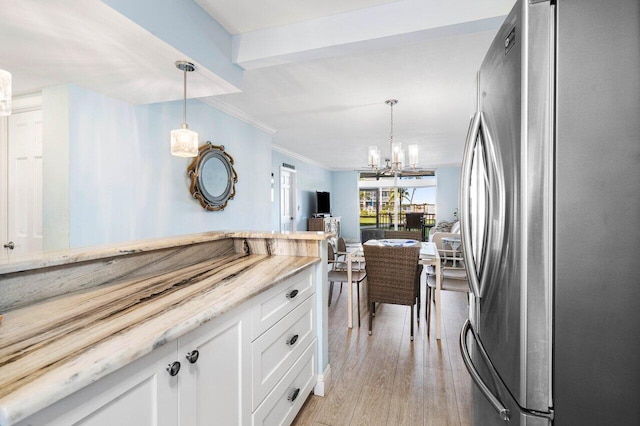 kitchen featuring light wood finished floors, white cabinets, light stone counters, freestanding refrigerator, and hanging light fixtures