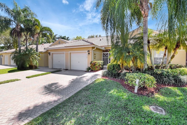 view of front of house with a garage, a tile roof, decorative driveway, a front lawn, and stucco siding