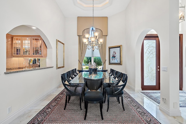 dining area with marble finish floor, a raised ceiling, a towering ceiling, an inviting chandelier, and baseboards