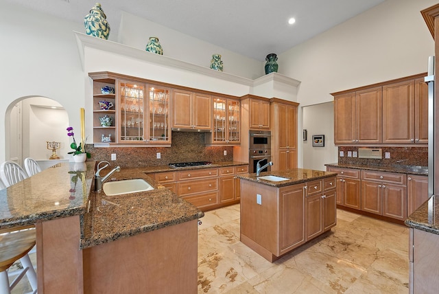 kitchen with arched walkways, decorative backsplash, a peninsula, a kitchen island with sink, and a sink