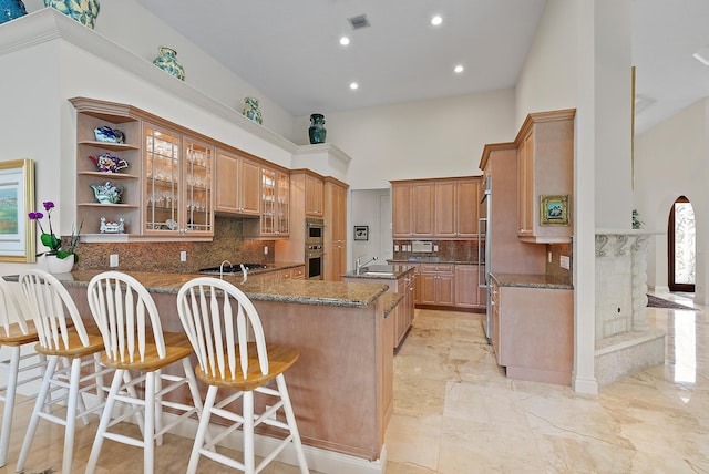 kitchen with visible vents, a towering ceiling, dark stone countertops, marble finish floor, and a kitchen bar