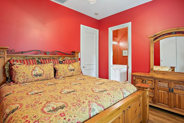 bedroom featuring wood finished floors, visible vents, and connected bathroom