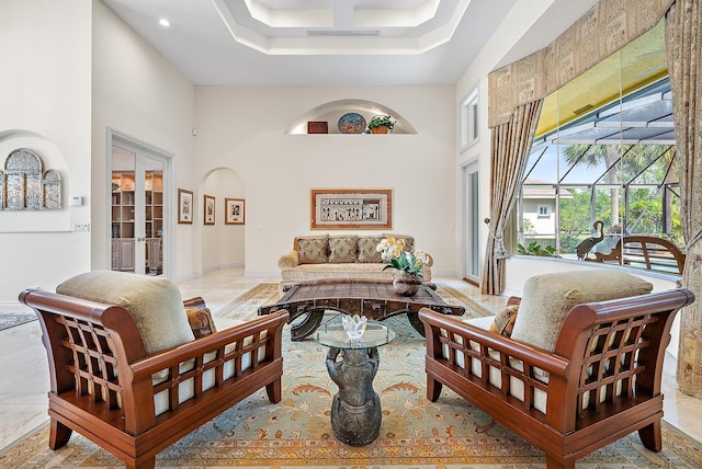 living area featuring visible vents, arched walkways, baseboards, a sunroom, and a high ceiling