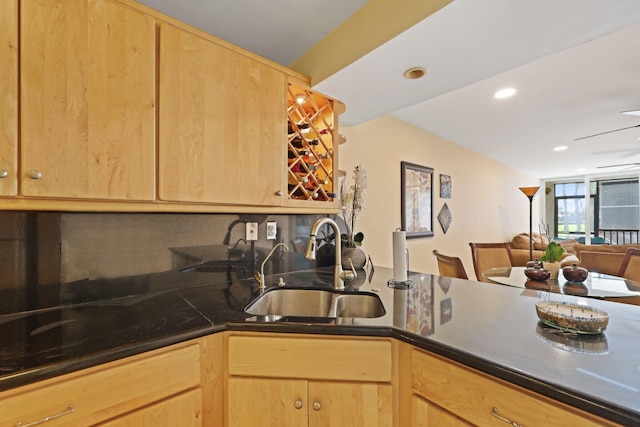 kitchen with dark countertops, light brown cabinets, open floor plan, and a sink