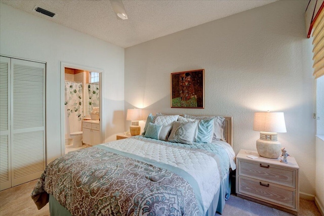 bedroom with ensuite bathroom, visible vents, a closet, and light carpet