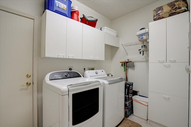 clothes washing area with cabinet space, a textured ceiling, and independent washer and dryer