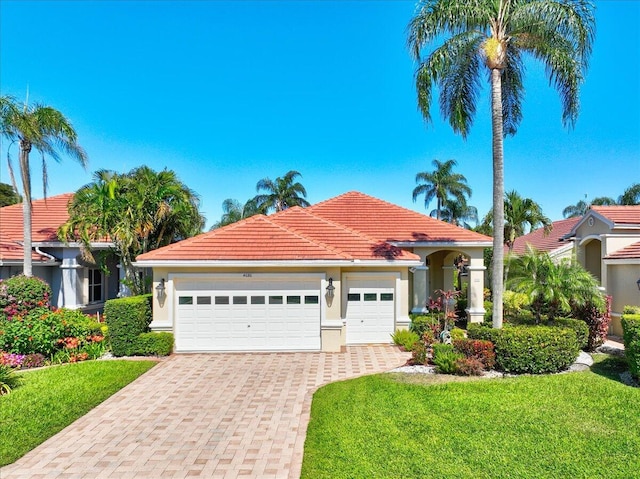 mediterranean / spanish home with stucco siding, a front lawn, a garage, a tile roof, and decorative driveway