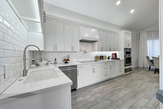 kitchen with lofted ceiling, a sink, appliances with stainless steel finishes, custom exhaust hood, and decorative backsplash