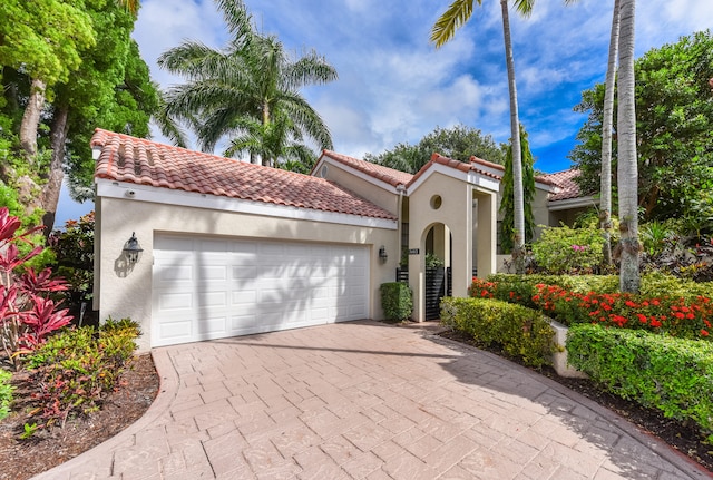 mediterranean / spanish-style home featuring a tiled roof, decorative driveway, an attached garage, and stucco siding