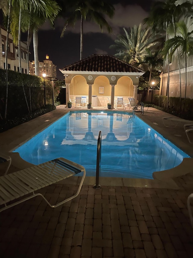 pool at twilight with a patio area, fence, and a community pool