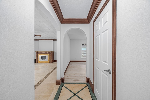 corridor featuring a textured wall, arched walkways, crown molding, and baseboards