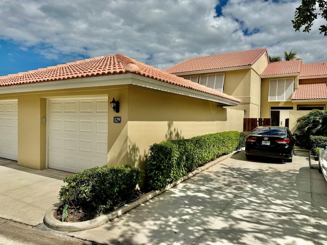 view of front facade with an attached garage, a tile roof, concrete driveway, and stucco siding