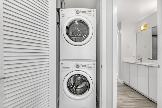 clothes washing area featuring laundry area, stacked washer / dryer, a sink, and wood tiled floor