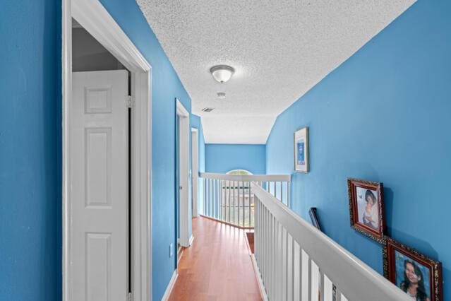 corridor featuring a textured ceiling, an upstairs landing, and wood finished floors