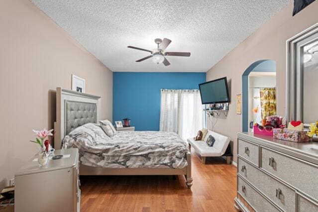 bedroom featuring arched walkways, ceiling fan, a textured ceiling, and wood finished floors