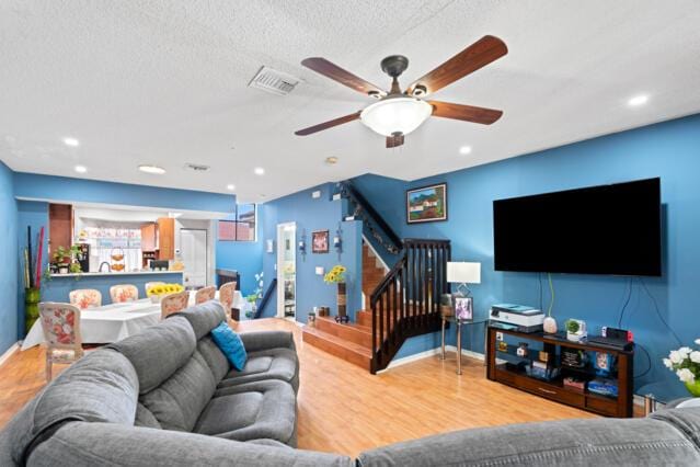 living room featuring baseboards, visible vents, stairway, wood finished floors, and a textured ceiling