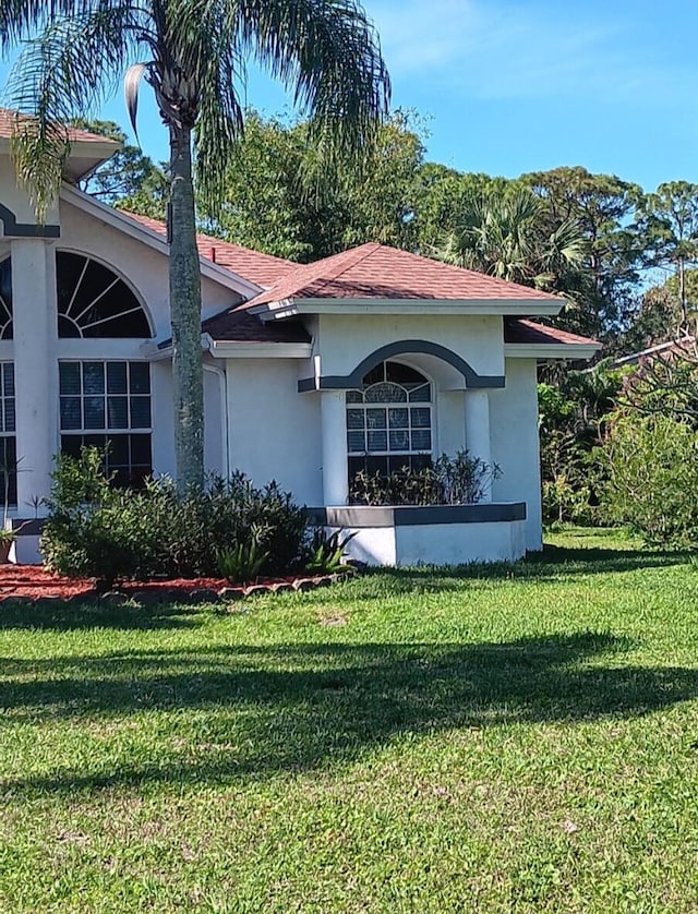 view of side of home with a yard, roof with shingles, and stucco siding