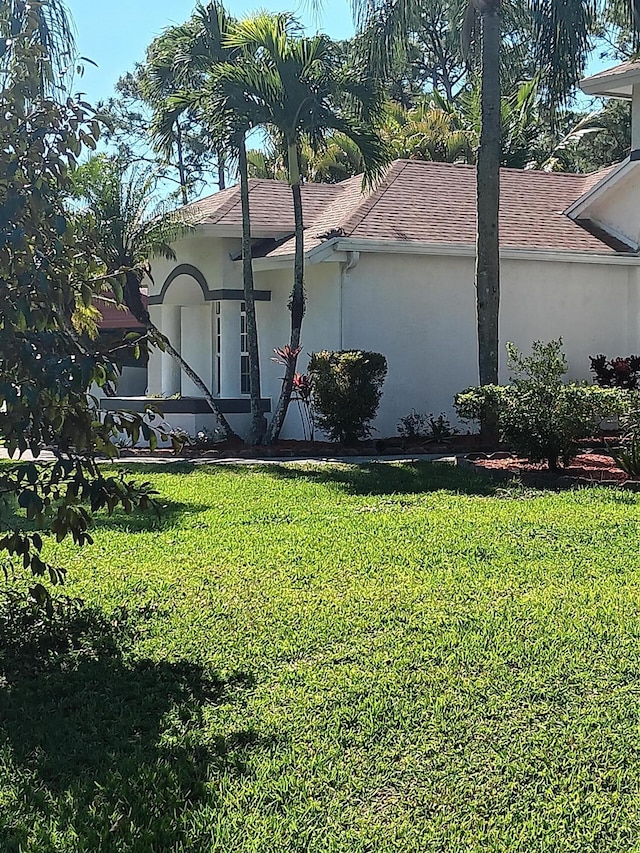 view of side of home with a yard, a shingled roof, and stucco siding