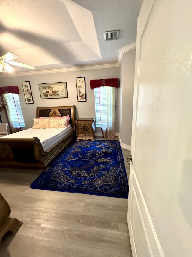 bedroom featuring crown molding, visible vents, ceiling fan, wood finished floors, and baseboards