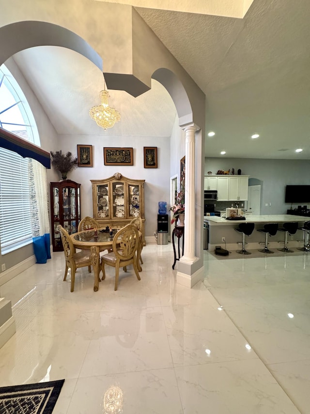 dining space featuring arched walkways, marble finish floor, decorative columns, a textured ceiling, and baseboards