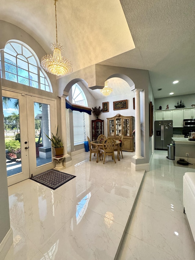 foyer featuring ornate columns, marble finish floor, arched walkways, and a textured ceiling