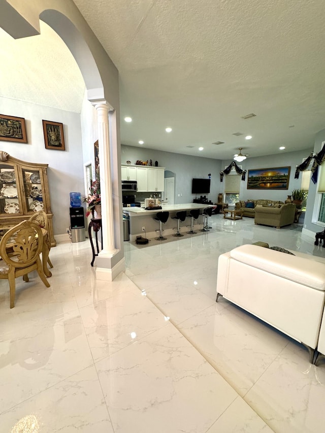 living area featuring arched walkways, marble finish floor, decorative columns, recessed lighting, and a textured ceiling