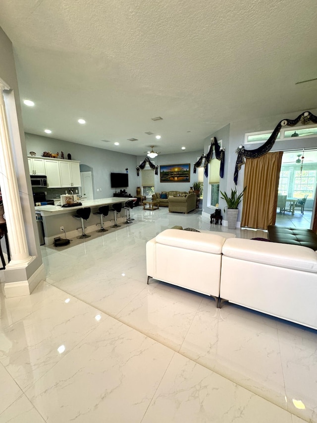 living room featuring marble finish floor, ceiling fan, a textured ceiling, and recessed lighting